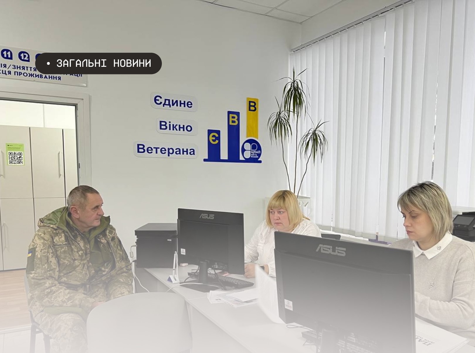 Чоловік у військовій формі сидить за робочим столом навпроти двох жінок-працівниць у світлому офісному кабінеті. На стіні позаду них розміщено напис «Єдине Вікно Ветерана» та логотип ЦНАПу на тлі синьо-жовтих геометричних елементів. Справа на передньому плані видно два чорні монітори, а на задньому плані — кімнатну рослину та білі вертикальні жалюзі на вікні.