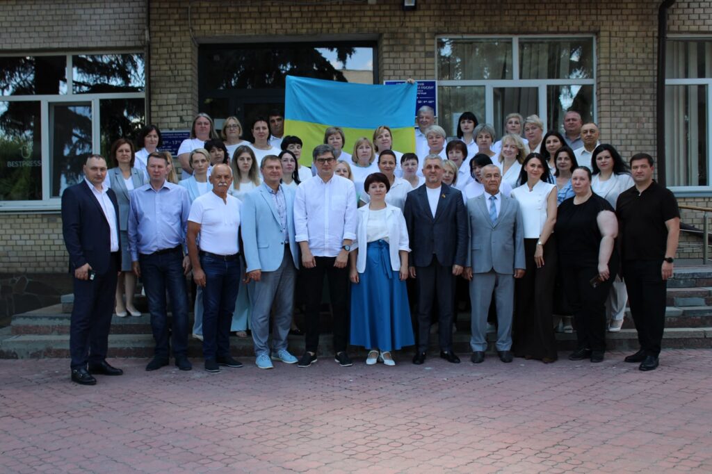 Групове фото учасників засідання колегії Головного управління Пенсійного фонду України у Київській області біля входу до адміністративної будівлі. На сходах стоять понад 40 людей, у центрі позаду них розгорнутий Державний прапор України.