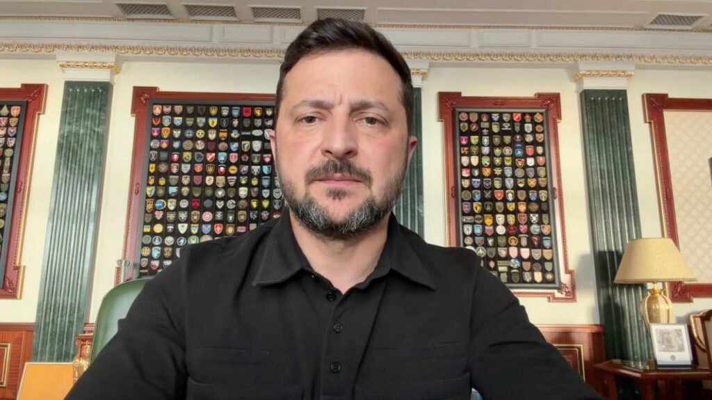 Президент України Володимир Зеленський сидить за робочим столом у своєму кабінеті. На тлі — декоративні панелі з колекцією військових шевронів.